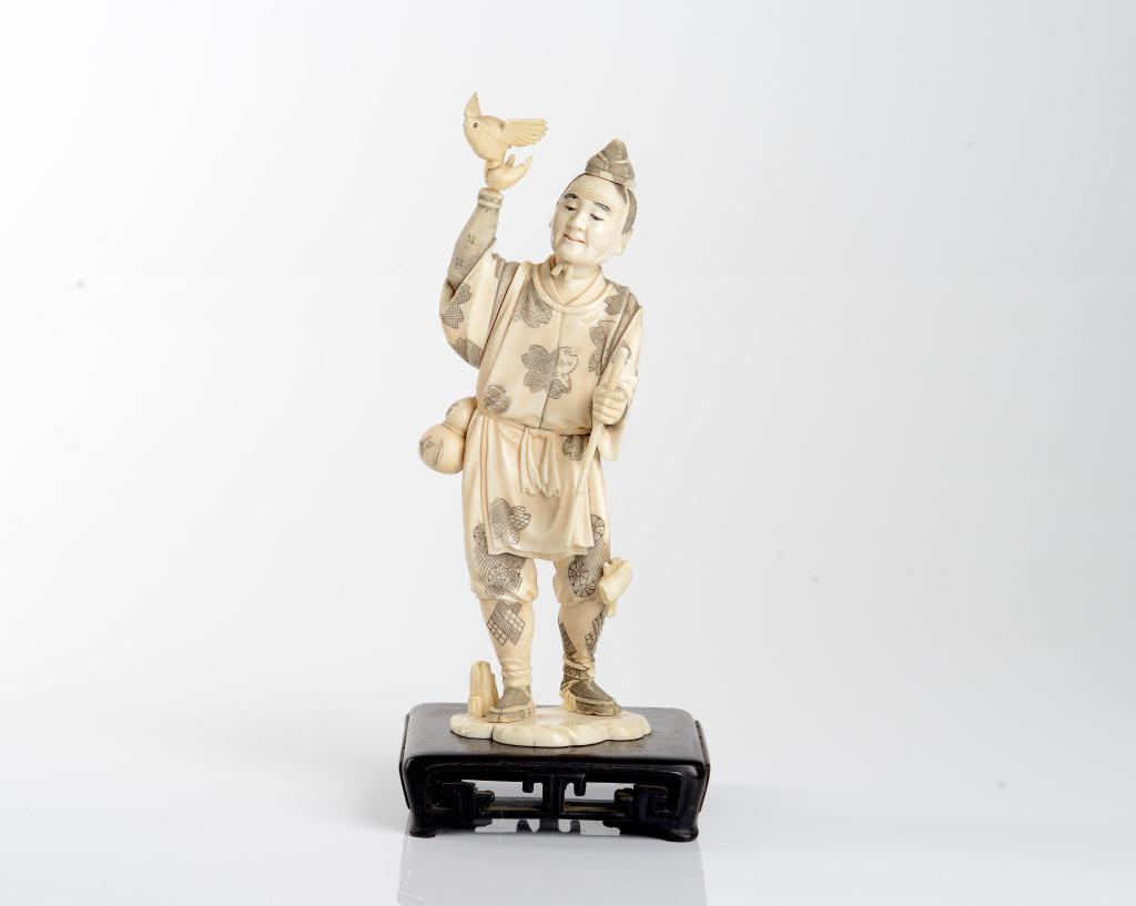 JAPANESE NATURAL CARVED OKIMONO FIGURAL GROUP: Of a standing man holding a staff and bird with decorative dress and gourd water basin. On Chinese hardwood stand, Meiji period. H of figure 24cm (9 1/2in)CITES