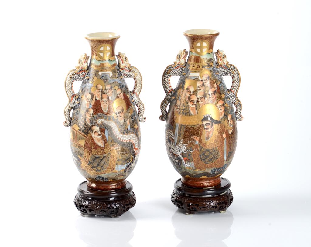 PAIR OF JAPANESE SATSUMA VASES: Meiji Era (1868-1912). A pair of vases painted with faces of men and white dragon handle detailing. Fixed to wood stand. H: 25.4 cm (10 inch.) Condition report available upon request