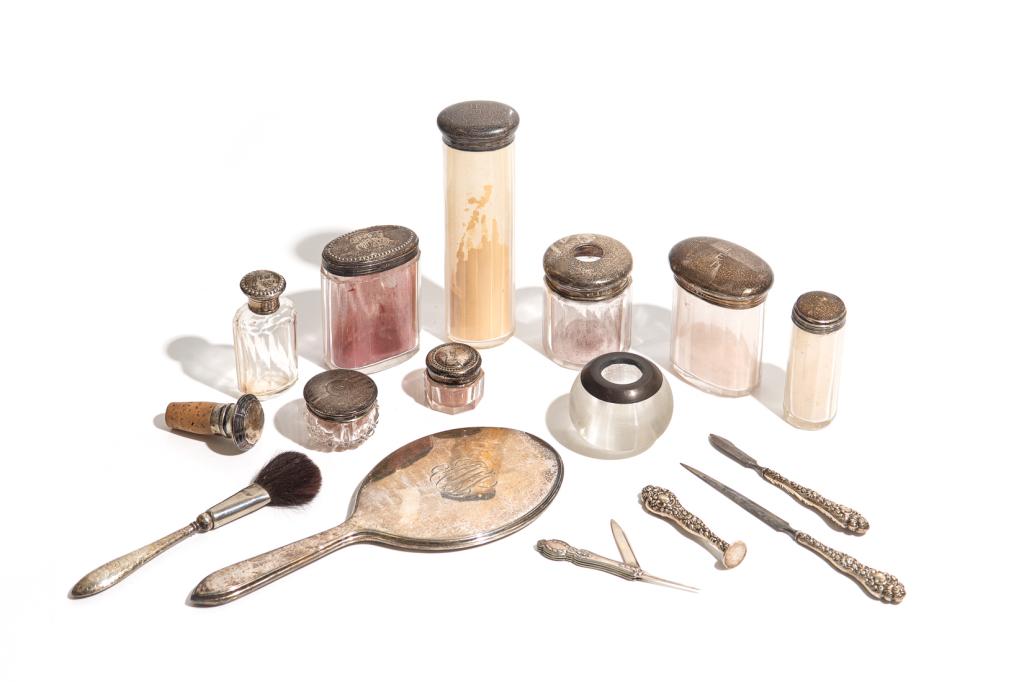 GROUP OF GLASS VANITY BOTTLES & SILVER ACCESSORIES: Comprising eight variously sized glass bottles with silver lids, silver wine stopper with cork, silver handled vanity set and hand mirror, and a small decorative striated glass globe candleholder. Con