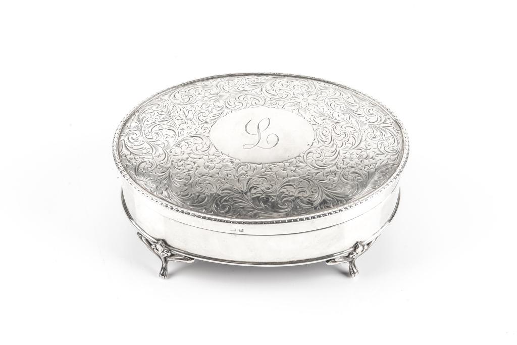 ENGLISH SILVER OVAL JEWELLERY BOX: With engraved scroll and foliate decoration surrounding a central cartouche with the initial L. Lined with velvet and raised on four feet. Synyer & Beddoes (Harry Synyer & Charles JosephBeddoes), Birm