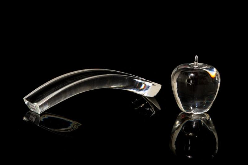 TWO GLASS PAPERWEIGHTS: A Steuben apple crystal paperweight (etched signature to bottom), together with an unsigned bridge form glass paperweight. L. of larger: 25.7 cm (10 1/8 in.)