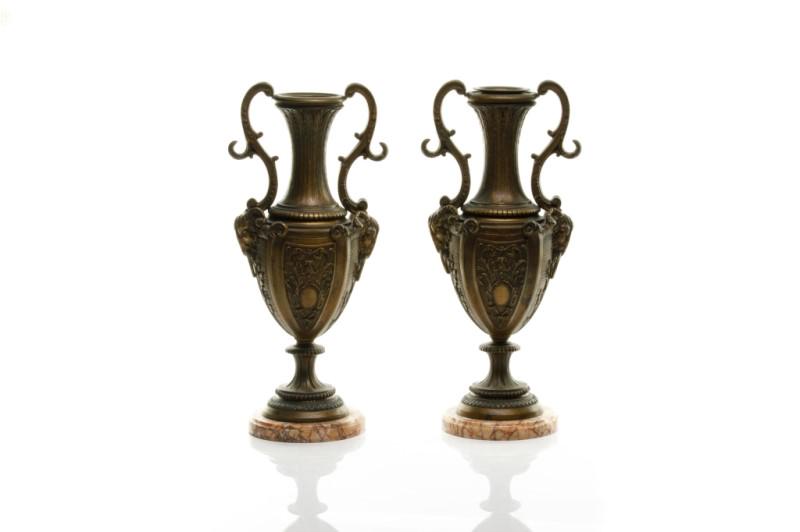 PAIR OF PATINATED SPELTER URNS ON MARBLE BASES: Likely French 19th C, and part of an earlier garniture set. With double figural rams head handles, foliate designs, and mounted on round red variegated marble bases. Signed Francois Moreau.H. 42.5 cm