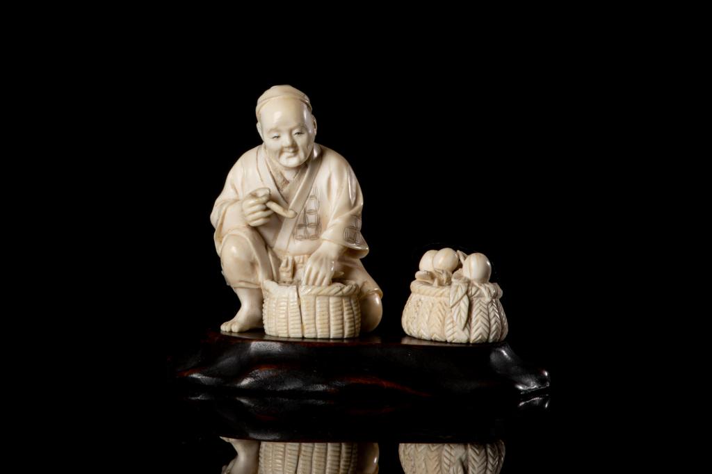 JAPANESE OKIMONO OF FRUIT VENDOR: 日本明治時期 象牙果販 Carved as a squatting man with two baskets of fruits. Meiji period. H. 6.5cm (2 1/2 in.) Bidders living outside of Can