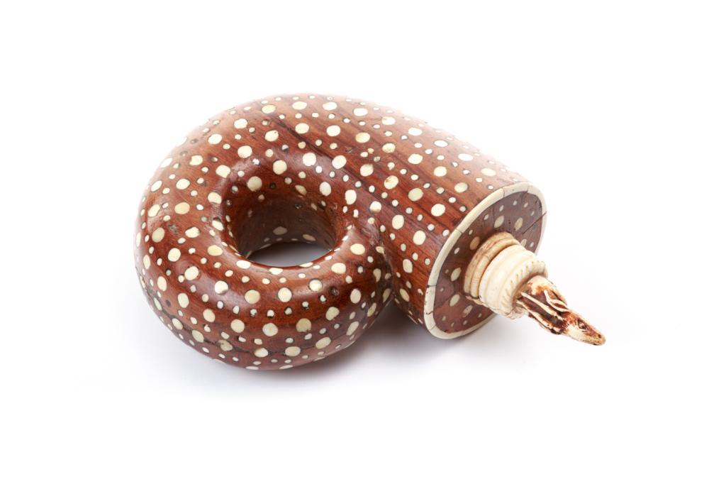 RAJASHTAN POWDER FLASK: A wood flask of the nautilus type inlaid with bone topped with an carved antelope. Height 19 cm (7.5 in.)