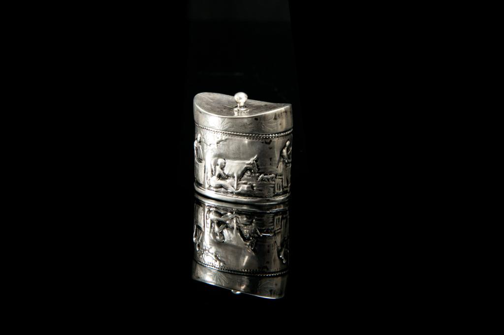 19TH C DUTCH SILVER MINIATURE CADDY FORM BOX, 19g: A small oval-shaped box with a hinged lid and rounded finial. Across the body is repousse decoration of farming and domestic scenes. Hallmarked to the underside of the lid with date letter for 1821 an