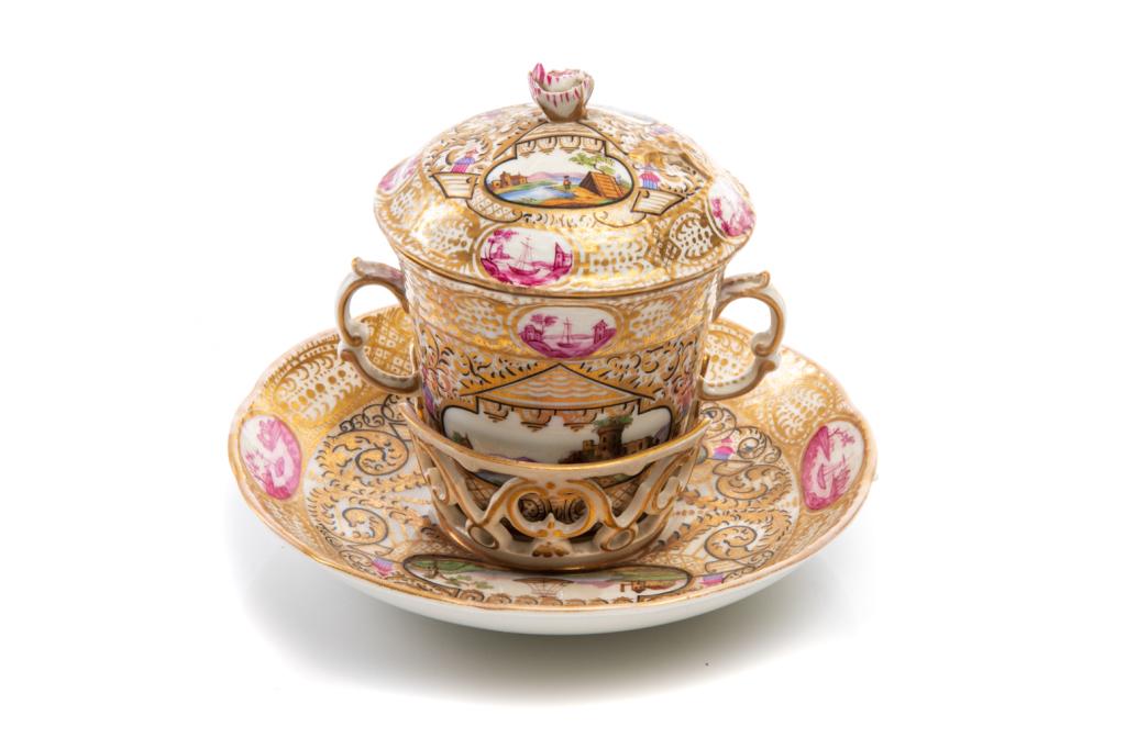 KPM PORCELAIN TREMBLEUSE CUP & SAUCER: Berlin, mid 19th c. Covered two handled chocolate cup & saucer with holder, hand painted landscape scenes and gilded detail. Rose finial on top of the lid. Blue under glazed mark on the underside of c