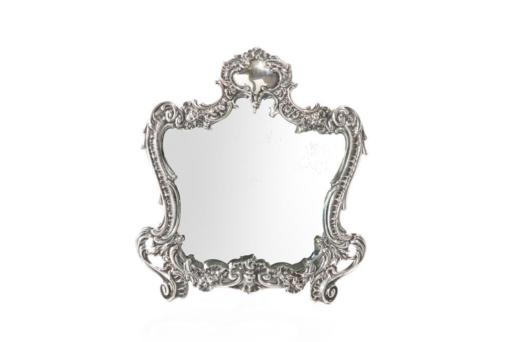 CONTINENTAL SILVER DRESSING MIRROR: A Rococo style vanity or dressing mirror with scrolling details and floral accents. Wood backing with brass locking mechanism. Hallmarked to base on the silver, partially obscured. H. 30.7 cm (12 in.)