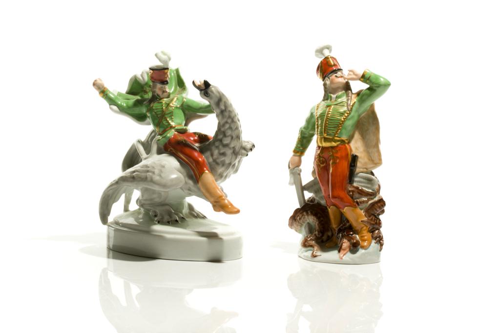 TWO HEREND PORCELAIN FIGURINES OF HUSSAR: Hungary, figures depicting Hussar in a green military style uniform, holding a sword after fighting a dragon and riding a mythical creature. Blue stamp marks on the underside of each. H. of larger: 22