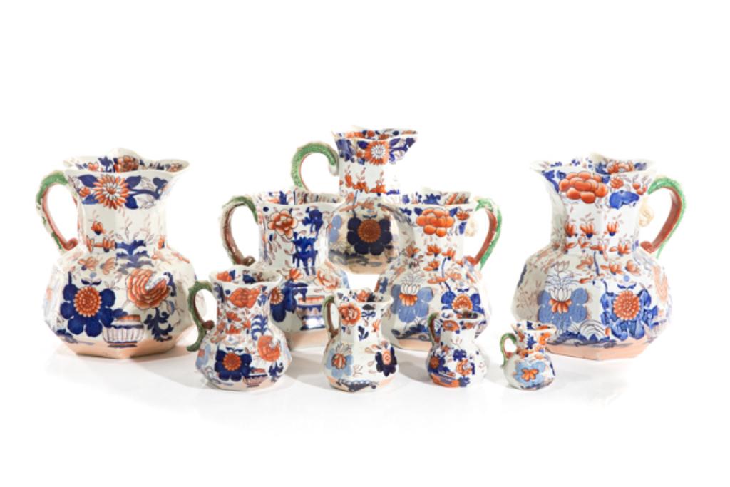COLLECTION OF ENGLISH IMARI MASON JUGS & PLATES: 19th century, hand painted with white ground and red & blue floral motifs throughout, ruffled rims, green painted serpent form handle on each. 14 pieces total, comprising two large pitchers, three mid