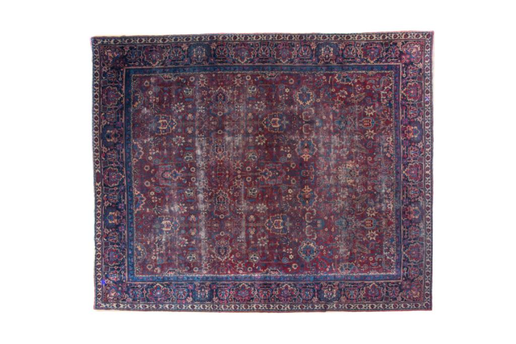 SEMI ANTIQUE PERSIAN WOOL CARPET: Possibly a Kerman, in a stylized arts and crafts design on a burgundy ground with navy border. Signed, with significant wear. 13ft x 10ft 6in