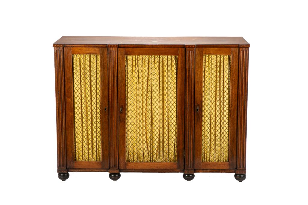 REGENCY THREE-DOOR CABINET WITH WIRE WORK FRONT: Mahogany cabinet with bands of satinwood inlay. Reeded trim on front and bun feet. Wire work fronted doors embellished with yellow silk lining. Interior with three shelves. English, early 19th C. H. 3