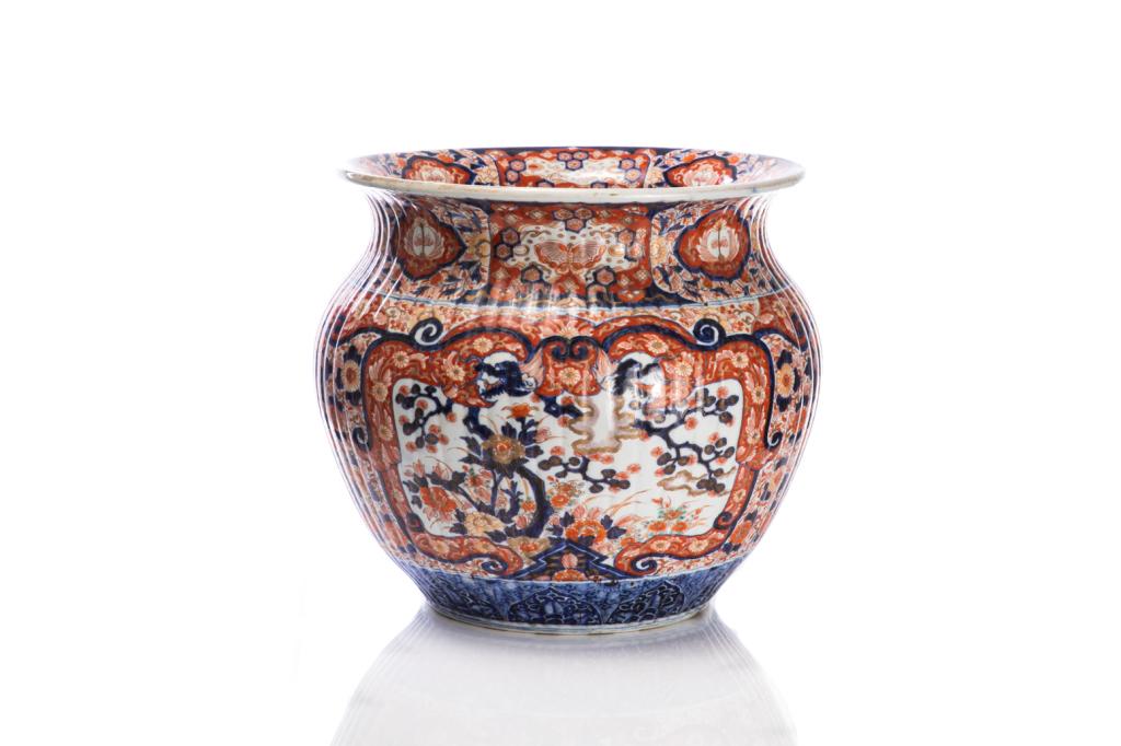 LARGE JAPANESE IMARI PORCELAIN JARDINIERE: Bulbous body with ribbed wall and outward flaring rim, painted with dragons and floral motifs. Meiji period. H. 41cm (16 in.) Provenance: From Chelster Hall Oakville, Ontario by order of the Estate Tr