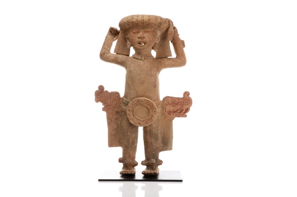 DECORATIVE TERRACOTTA MAYAN STYLE FIGURE: 20th century interpretation of an ancient pottery figure. Stylized hollowed male nude with raised hands, dressed in head piece, jewellery and with an abstract shield form belt. Together with a custom 