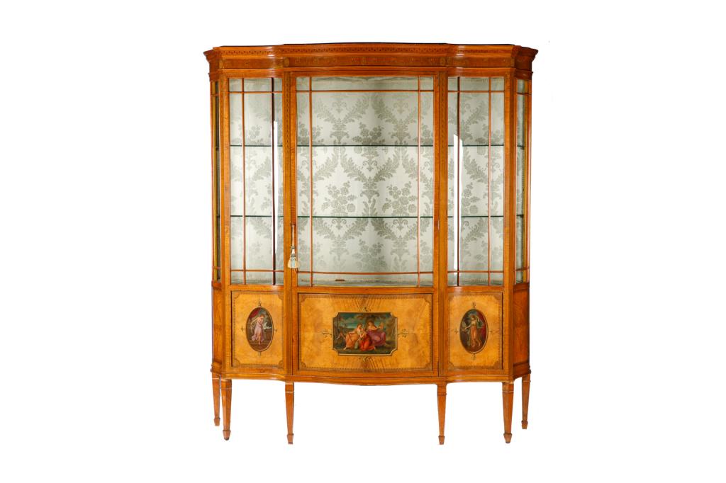 EDWARDIAN SATINWOOD DISPLAY CABINET: Serpentine form with tapered legs. Marquetry inlay with painted roundels and scenes. Interior with contemporary upholstery, two glass shelves. Lower cupboard. English, early 20th c. H. 78" W. 66" D. 2