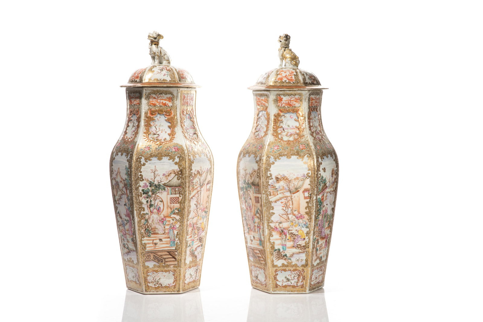 PAIR CHINESE EXPORT FAMILLE ROSE PORCELAIN URNS: Painted on each facet with elaborate scenes of figures in garden landscapes, within rococo style gilt borders. Cover with similar painting and a molded seated fu lion finial. Qing dynasty, late 18th c