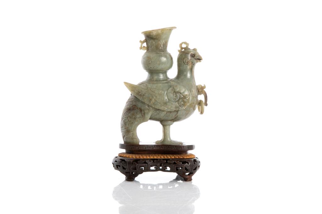 CHINESE JADE CARVED PHOENIX AND VASE WITH STAND: Overall in grey celadon tone with russet and black inclusions. Carved as a standing phoenix figure with a vase on back. With fitted silver inlaid wood stand. Height of jade: 15cm (6 in.) Height on sta