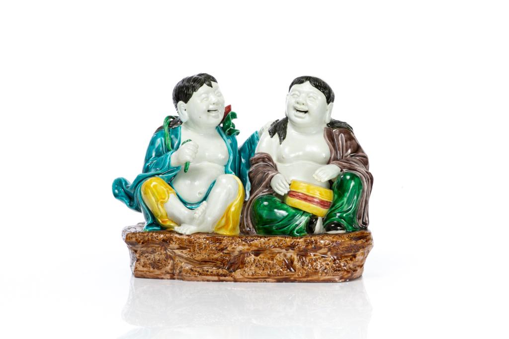 CHINESE REPUBLICAN PORCELAIN HEHE TWIN FIGURE: Both figures seated on a rock platform with clothing glazed in turquoise, aubergine, and yellow. Impressed You Lin Ji mark to base. H. 28cm (11 in.)