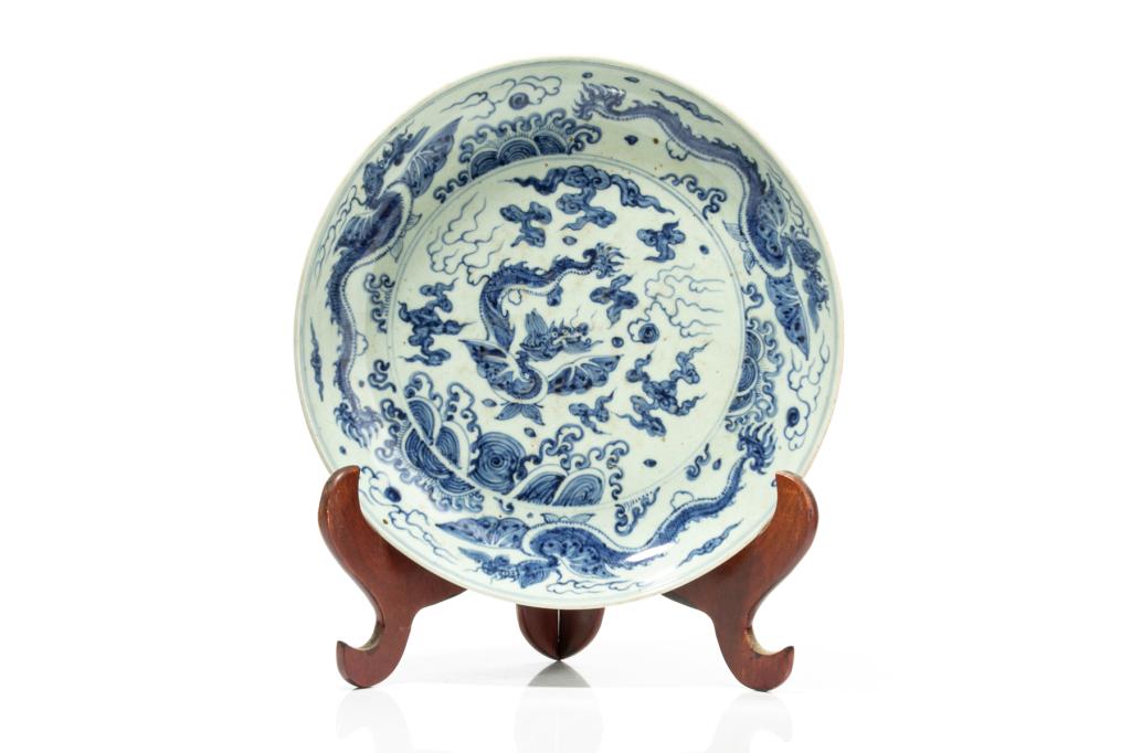 CHINESE BLUE & WHITE PORCELAIN DRAGON DISH: Painted with a central circular scene of a winged dragon amongst clouds and waves, and further dragons circulating the elevated to both sides. Ming dynasty. Dia. 34cm (13 1/4 in.)