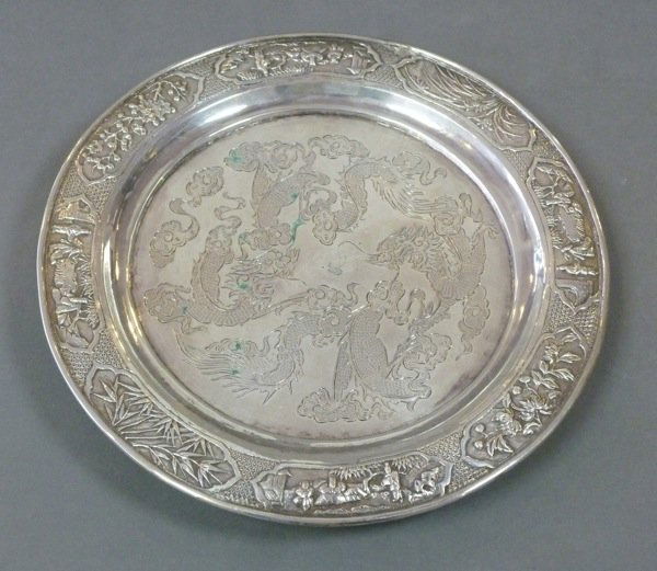 CHINESE EXPORT SILVER SALTER WITH DRAGONS: Chinese export silver circular salver on three feet. The center engraved with two dragons and the border with panels of people and various foliage. Maker 'HHC'. D 22 cm (8 5/8 in). 305 grams.