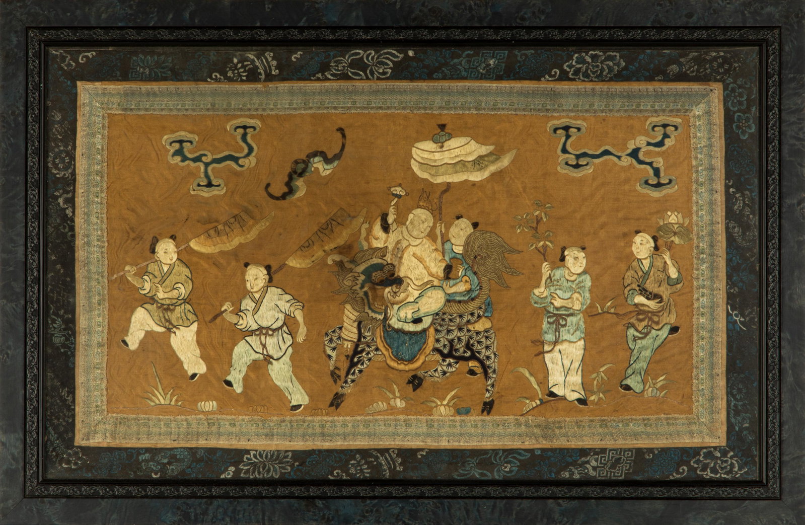 CHINESE EMBROIDERED SCENE OF FIGURES: Chinese, Qing dynasty, a figure riding a qilin (mythical beast) with attendant holding umbrella over him, further attendants holding flowers and banners. Having bat and stylized clouds in sky on faded