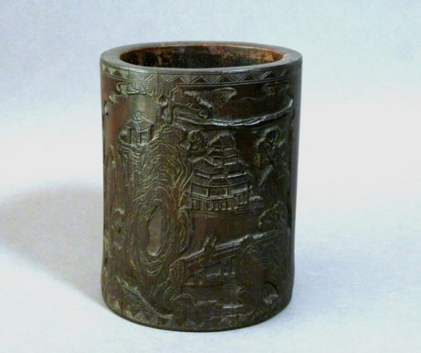 CHINESE 19th CENTURY CARVED BAMBOO BRUSH POT: Chinese bamboo brushpot carved with a landscape of mountains and buildings on one side and a cartouche of stylized calligraphy and writing on the other. Dark brown patina, 19th century. H 15.7 cm (6 1