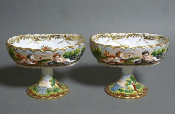 PAIR OF NAPLES PORCELAIN FOOTED DISHES: Pair of Capodimonte hand painted porcelain footed dished with raised putti and floral centre. H 9 cm. (3 1/2 in.).