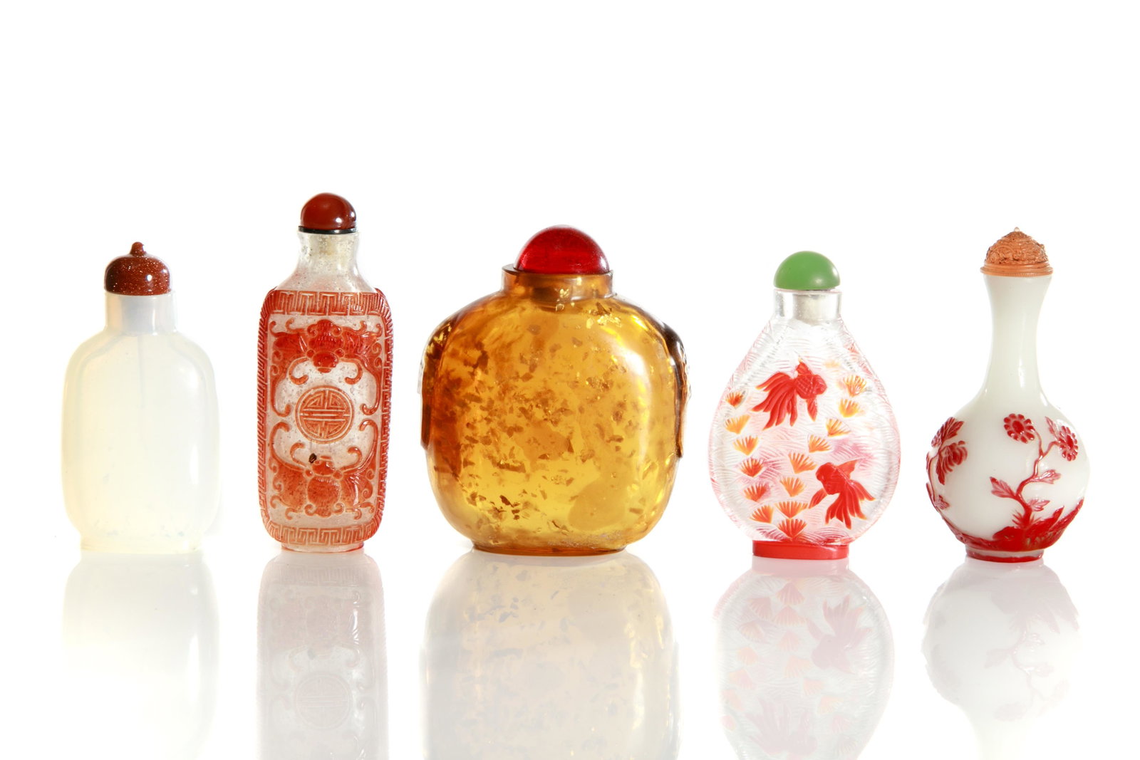 FINE CHINESE GLASS SNUFF BOTTLES: Chinese, 19th/20th century. Three with red Peking glass, one featuring bats and shou symbols carved in low relief; a white glass bottle, together with a gold flecked bottle. With a variety ofstoppers.
