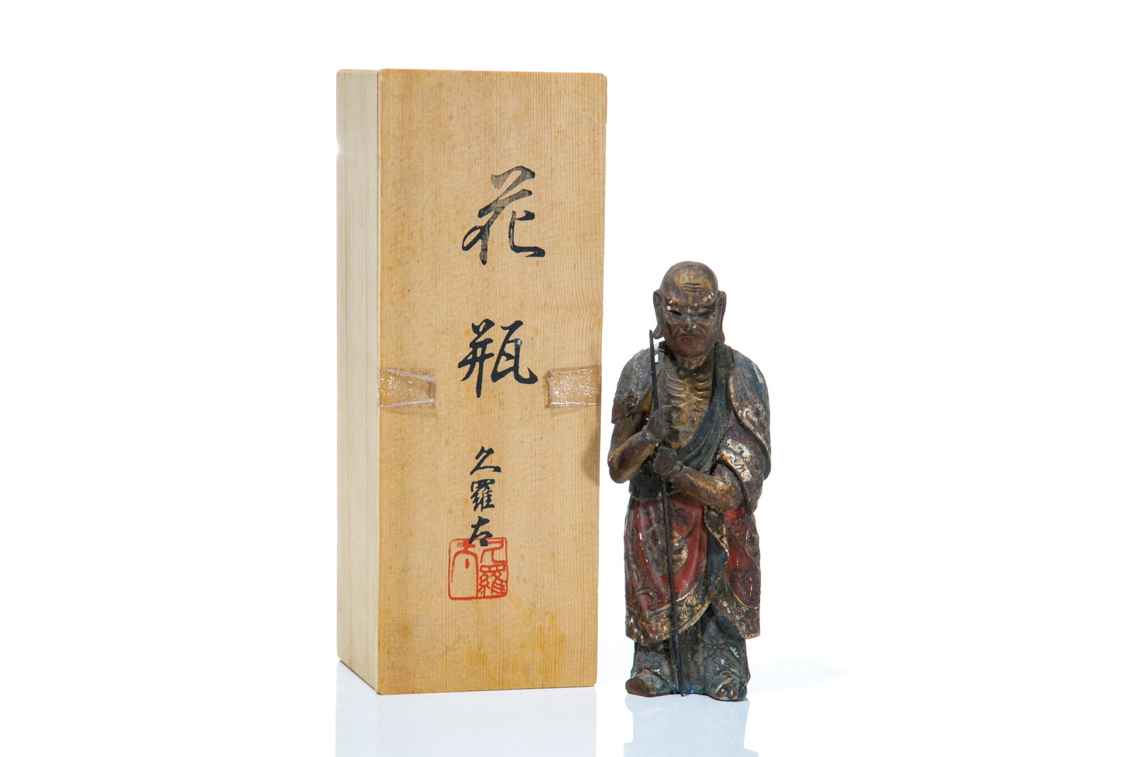 JAPANESE PAINTED WOOD CARVING OF FIGURE: In wood box, a standing wood temple figure with emaciated ribs, holding rod, painted in red, white and gold, having inlaid glass eyes. Covered in soot from incense. H. 19 cm (7 1/2 in.)