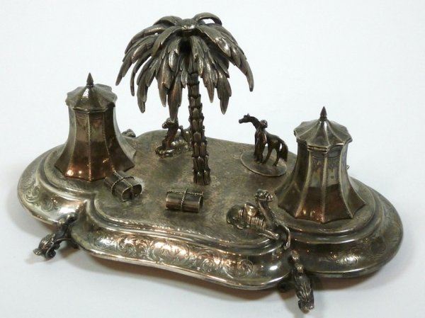 VICTORIAN ENGLISH SILVER PLATE FIGURAL INKSTAND: Fine English silver plate inkstand made as an middle eastern encampment. Decorated with figures of camels, a man with a horse , trunks and tents as the inkwells. Crested. Mid 19th century. L 24 cm (9 