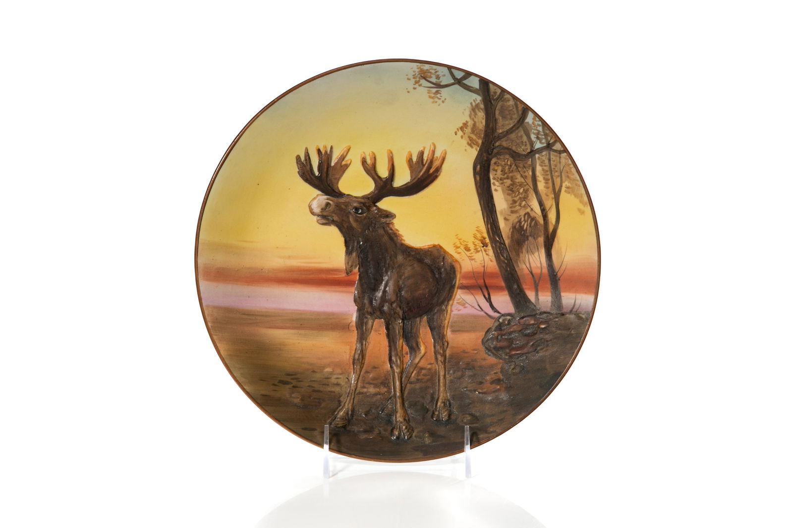 MOOSE NIPPON PORCELAIN WALL PLAQUE: Mold blown, hand-painted moose in relief, landscape scene in background, brown, pink, red, and yellow gradient. Japanese, green M in wreath mark, early Noritake. Dia. 27 cm (10 5/8 in.)