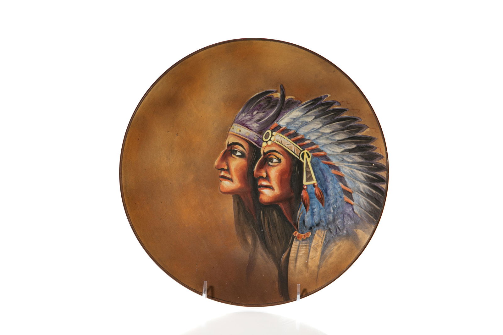 AMERICAN INDIAN NIPPON PORCELAIN WALL PLAQUE: Mold blown, hand-painted Nippon porcelain wall plaque of two American Indians wearing headdresses in relief, brownish orange background. Japanese, green M in wreath, early Noritake. Dia. 27 cm (10 5/8
