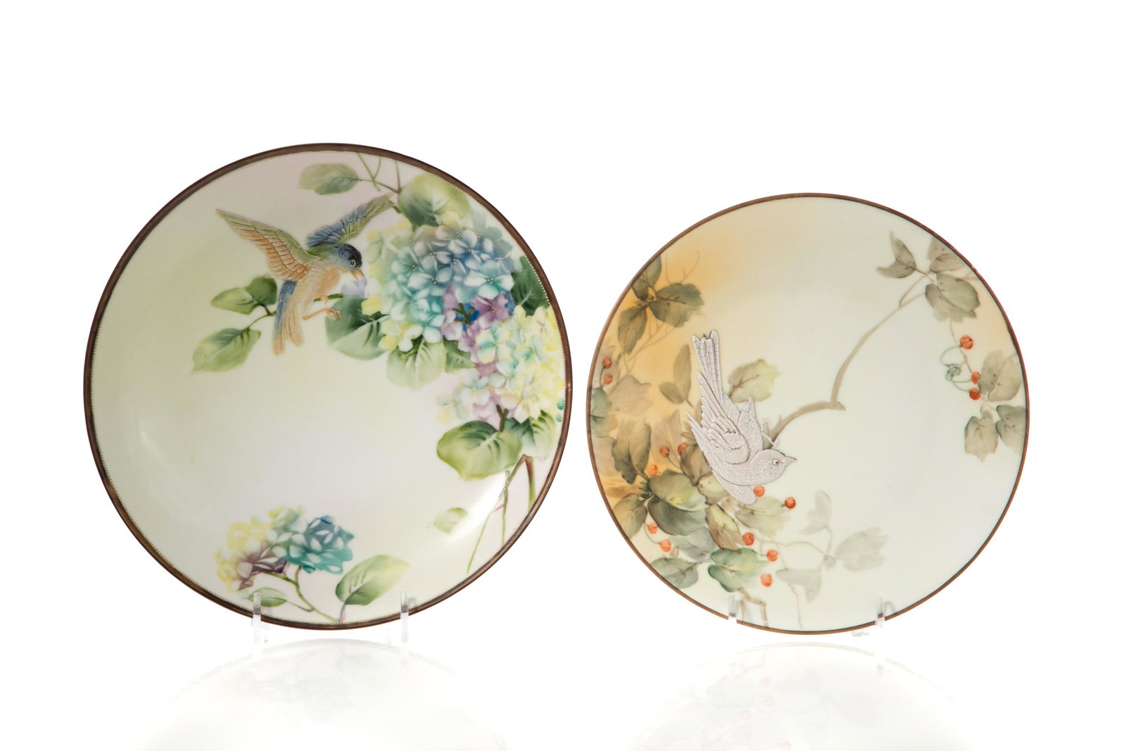 TWO NIPPON PORCELAIN WALL PLAQUES: Two hand-painted Nippon porcelain wall plaques featuring birds in relief resting on branches, spring floral scenes in background. Japanese, green maple leaf mark. Dia. of largest: 22 cm (8 5/8 in.)