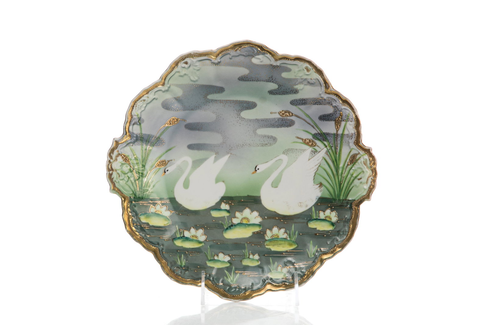 NIPPON HAND PAINTED & GILDED PORCELAIN PLATE: A hand-painted Nippon porcelain and gilt plate with scalloped edge, depicting two swans swimming in a pond among lily pads and reeds. Emulating a Royal Bayreuth, well-known pattern. Japanese, OCCO and