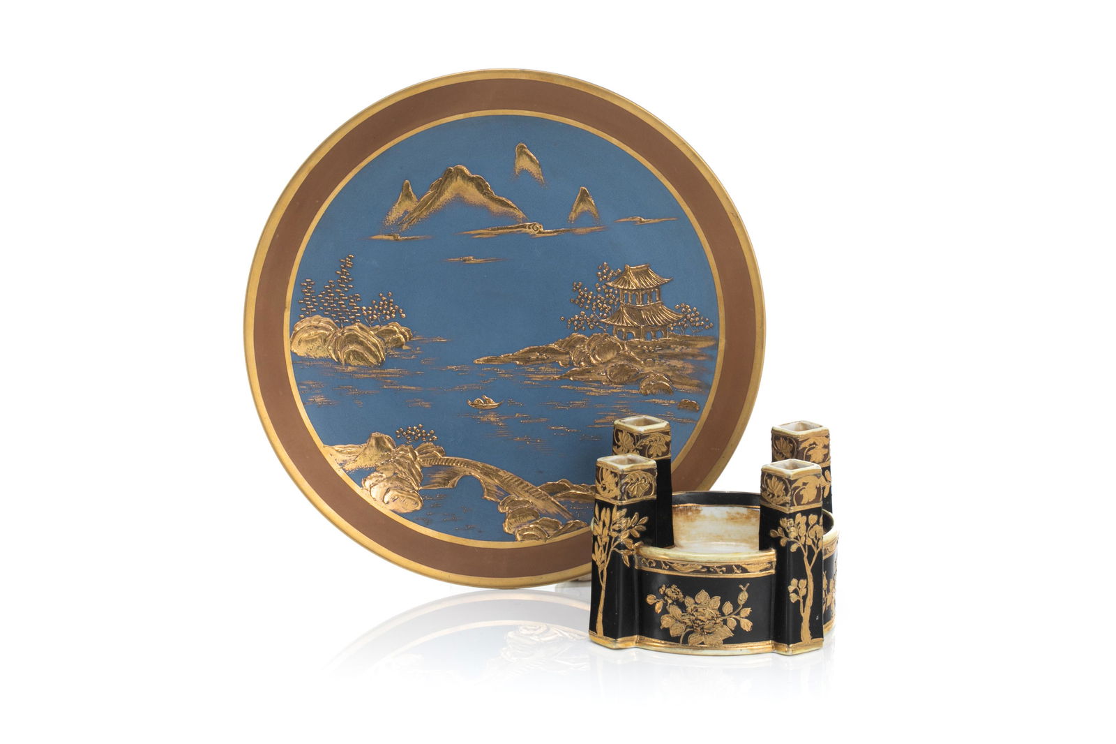 NIPPON PORCELAIN WALL MOUNT & FLOWER FROG: Blue matte glazed ground with gilded moriage landscape scene. Together with a black matte glazed ground with gilded decoration. Japanese, green maple leaf mark, early Noritake. Dia. of wall mount: 25.