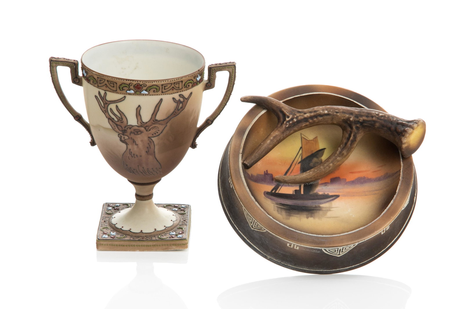 NIPPON TWO HANDLED MORIAGE CUP & ANTLER ASHTRAY: Brown matte glaze trophy cup with moriage stag and decoration. Together with a mold blown antler ashtray with hand painted scene of a sailboat. H. of cup: 15 cm (5 7/8 in.)