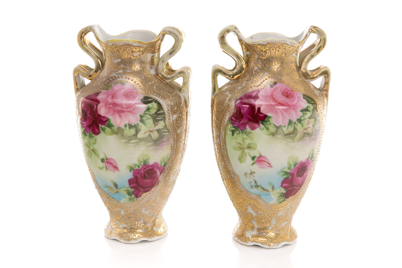 PAIR OF NIPPON TWO HANDLED PORCELAIN VASES: Two matching baluster form high gloss vases featuring hand painted scenes in the center; one side with roses; the opposite of a house beside a lake, surrounded by gilded decoration. Japanese,green I. 
