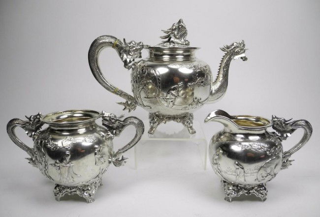 FINE CHINESE EXPORT SILVER TEA SET DRAGON: Comprising a teapot, cream jug and sugar bowl. Each with cast dragon handles and applied figures in a landscape. Makers mark CS (backwards 'S'). China, 19th century. Length of teapot 24 cm (9 1/2"). W
