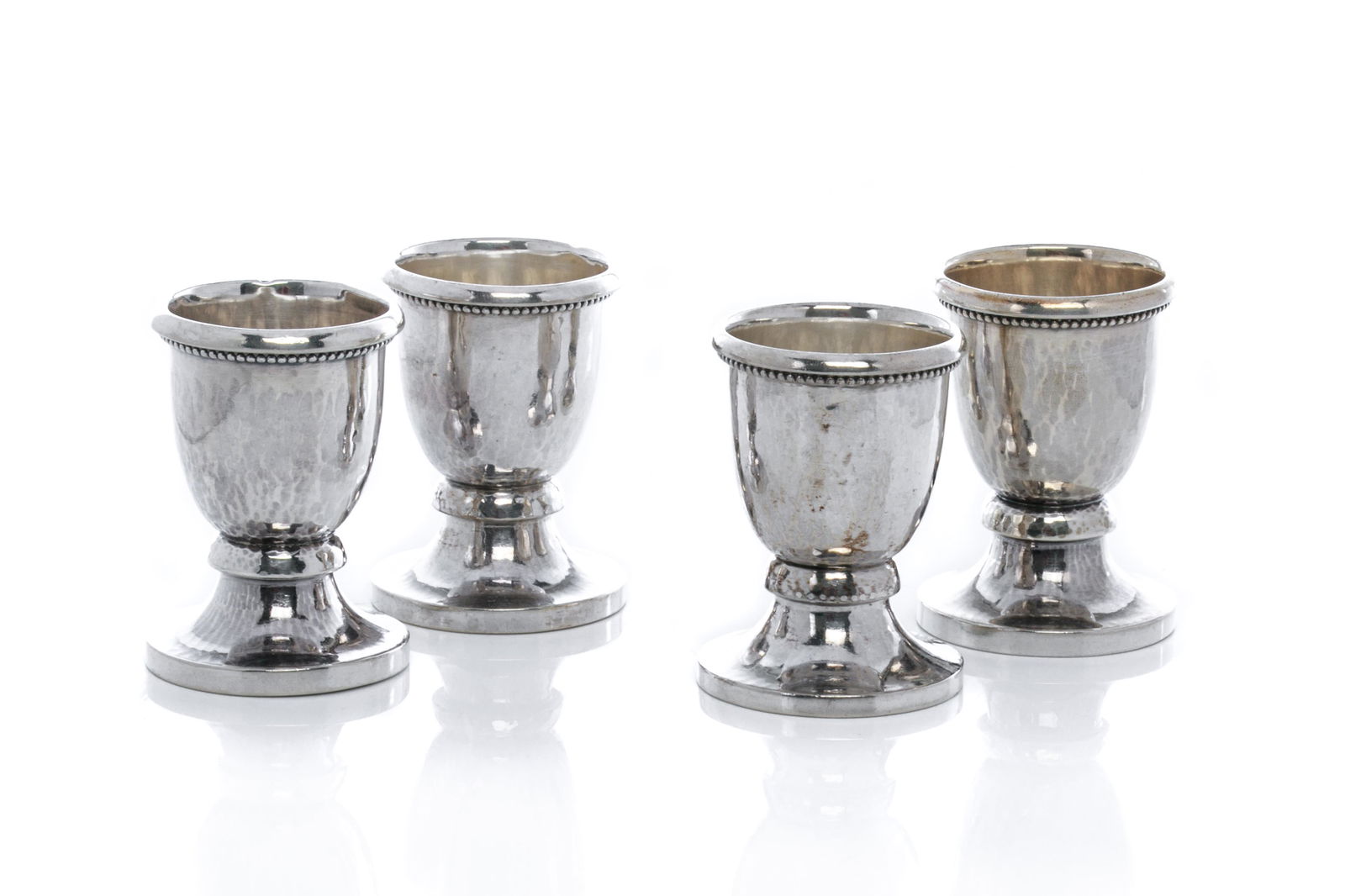 FOUR GEORG JENSEN SILVER EGG CUPS, no. 128: Four Georg Jensen sterling silver egg cups, rolled rim with beaded motif underneath, knoped and flared foot with hand hammered patterning throughout, numbered 128. Jensen hallmarks to base circa 1915-