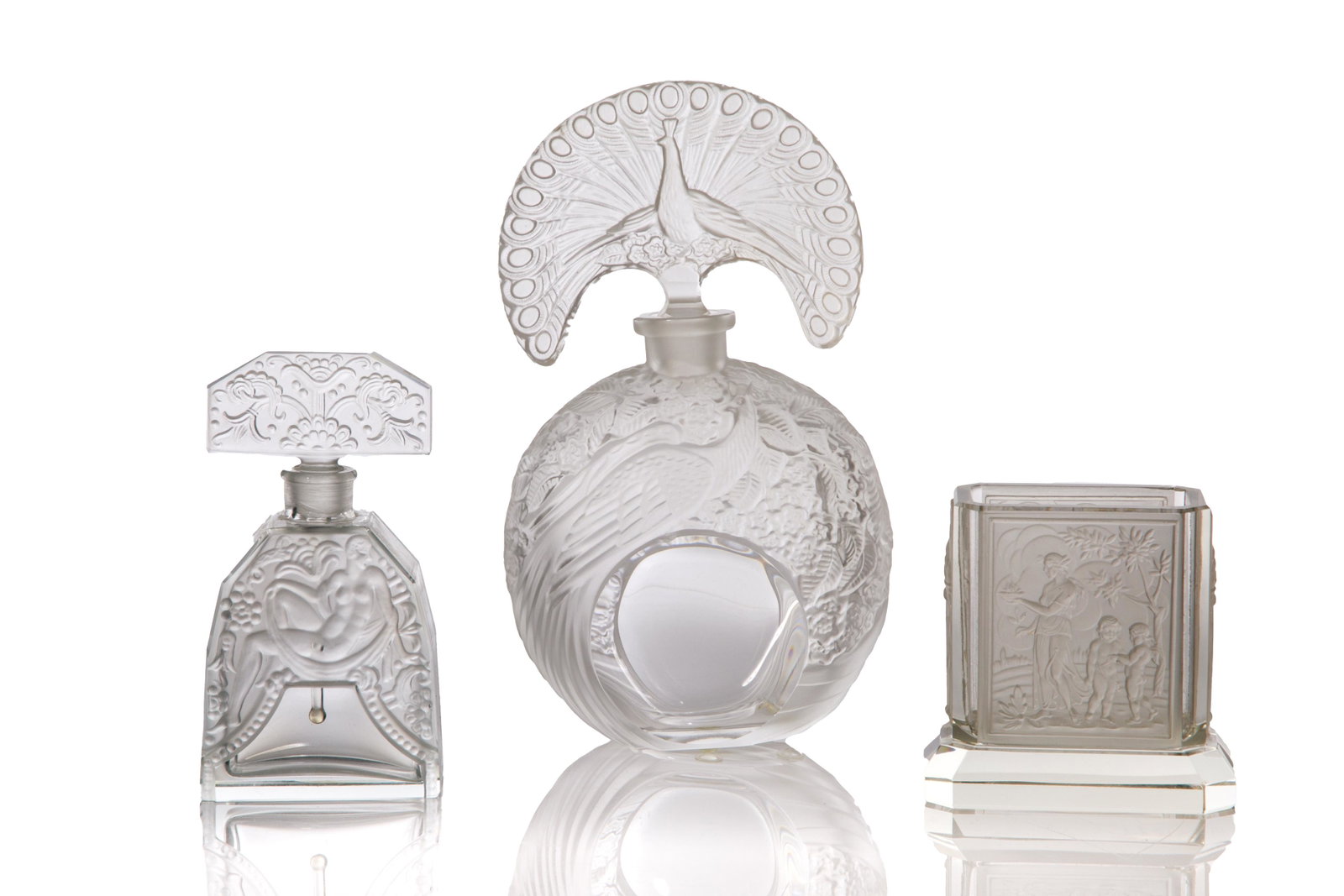 THREE ART DECO GLASS VANITY PIECES: Including a perfume bottle with a peacock stopper, another perfume bottle with molded nude, and a cigarette holder with molded classical scenes. In clear and satin glass. H. of tallest: 18.8 cm (7 3/8