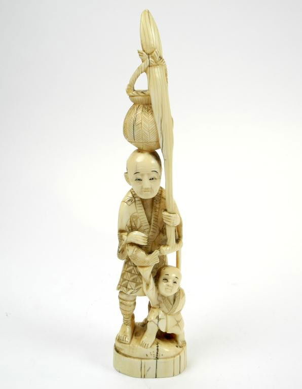 JAPANESE IVORY FIGURE OF FISHERMAN AND SON: Man carries in left hand a paddle with a bamboo basket tied over it, the child stands before him with right hand holding up a fish and left hand with a landing net. With black inlaid, base marked and