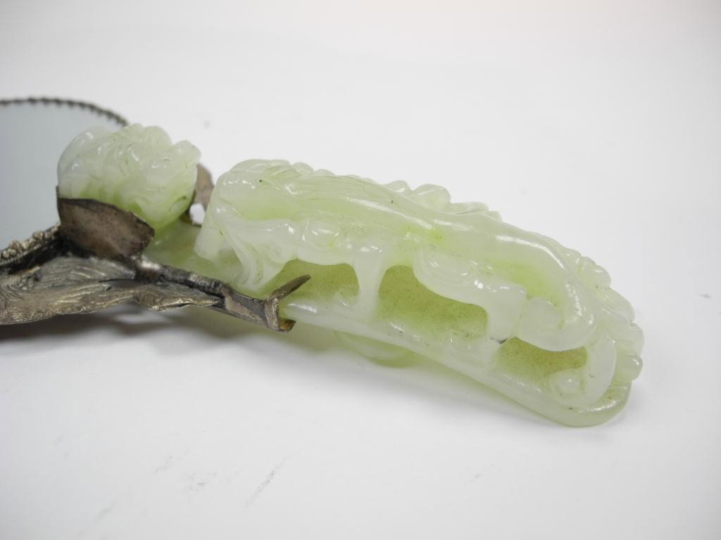 CHINESE GREEN JADE BELT HOOK MOUNTED HAND MIRROR: Jade belt hook with relief carved dragon mounted on a silver plated mirror. L. 22cm (8.6 in)
