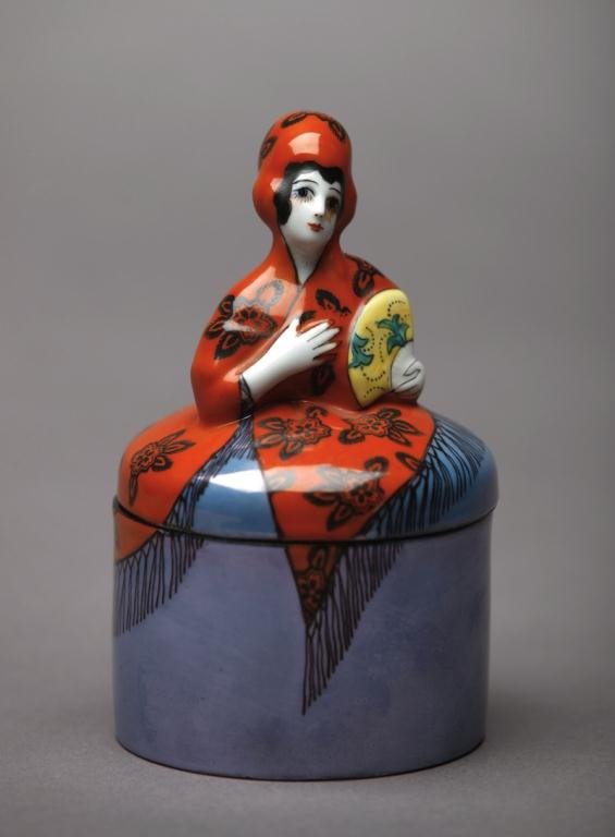 NORITAKE FIGURAL DRESSER JAR: Of a Spanish lady in an orange shawl and blue lustre skirt. Green M-in-Wreath. H 14 cm. (5 1/2 in.)