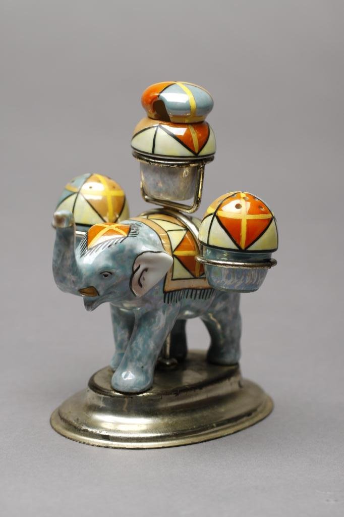NORITAKE UNUSUAL FIGURAL CONDIMENT SET: Polychrome lustre elephant on a metal stand holding three miniature condiment pots. Shakers marked Japan. H 14 cm. (5 1/2 in.)
