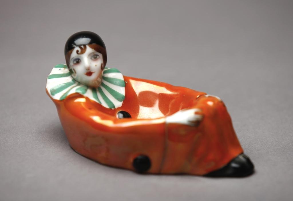 NORITAKE FIGURAL TRINKET DISH: Pierrot dish in a orange lustre suit. Red M-in-Wreath, 27.3. L 12.5 cm. (4 3/4 in.)