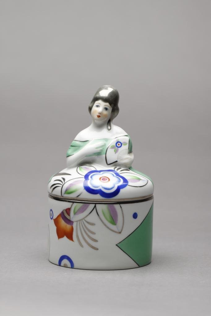 NORITAKE FIGURAL DRESSER JAR: Lady with silver lustre hair and Art Deco pattern on green dress (crack to base). English Spoke mark, H 14.4 cm. (5 5/8 in.)