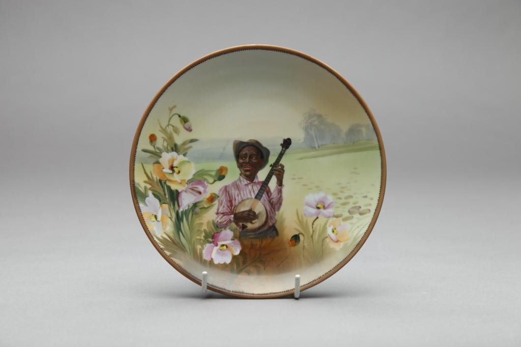 NIPPON HAND PAINTED PLAQUE: Of an African American playing banjo in the field. Green M-in-Wreath, Dia 19.5 cm. (7 3/4 in.)