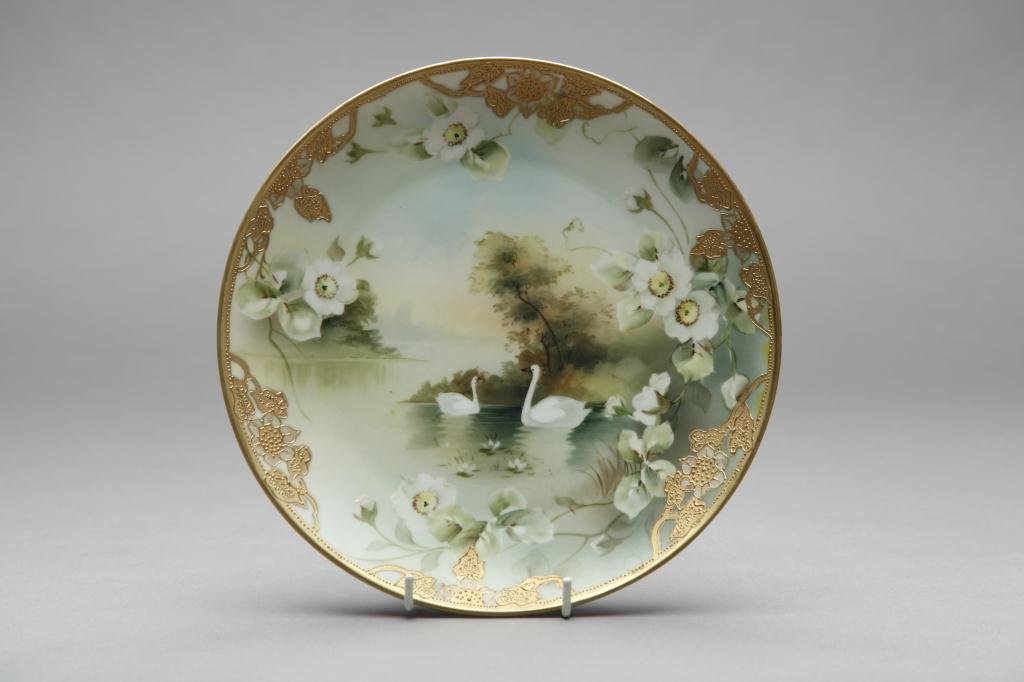 NIPPON HAND PAINTED PLAQUE: With swans in the lake, floral and applied gilt border. Blue Maple Leaf, Dia 25.3 cm. (10 in.)