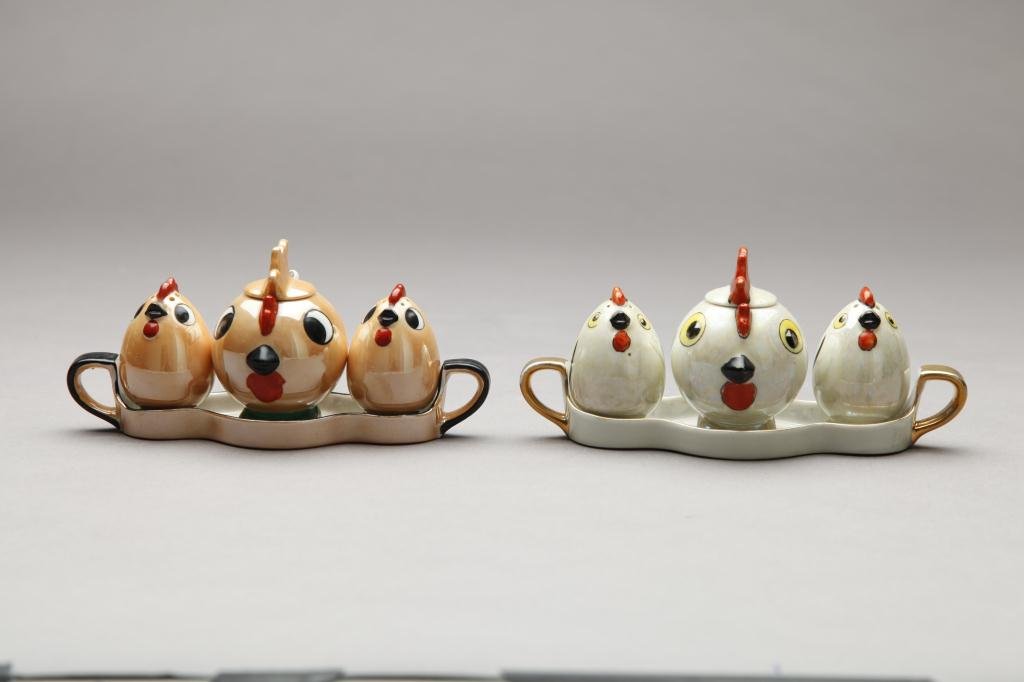TWO NORITAKE FIGURAL CONDIMENT SETS: Each a three piece chicken set with tray in white pearlized and caramel lustre (minor chip). Green-M-in-Wreath, W of tray 18.7 cm. (7 5/8 in.) On caramel lustre chick has a small chip to foot