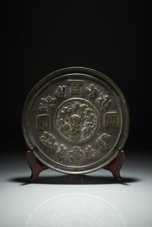 KOREAN BRONZE HAND MIRROR: Alternating pattern of boys and fortune symbols with kylins in the centre. Dia 22 cm. (8 3/4 in.) Provenance: from the collection of Mr. Abraham Abraham of The Jade Shop, Toronto.