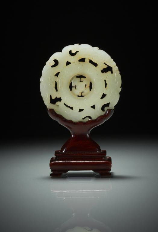 CHINESE CARVED JADE BI-DISC: Of pale celadon stone, carved in centre with a mobile disc and cloud relief, bordered by four stylized dragons. Dia. 6.1cm (3.5/8 in.) Provenance: from the collection of Mr. Abraham Abraham of The Jad